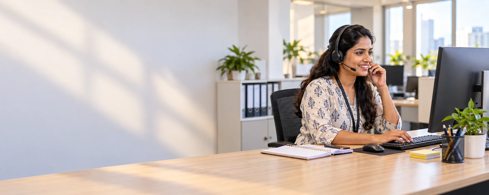 A smiling support executive wearing a headset at her desk in a bright office